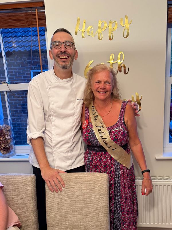 Chef Alpay beside a guest wearing a birthday sash at her 60th birthday celebration