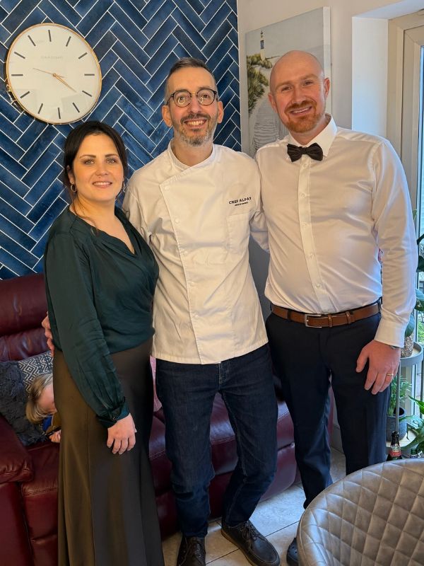 Chef Alpay posing with two guests in front of a blue tiled wall